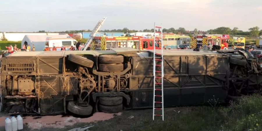 Einsatzkräfte der Feuerwehr stehen an der Unfallstelle neben dem verunglückten Bus. Der Bus überschlug sich zwischen den Anschlussstellen Leipzig-West und Bad Dürrenberg. Anschliessend blieb das Fahrzeug auf der Seite liegen. Foto: Jan Woitas