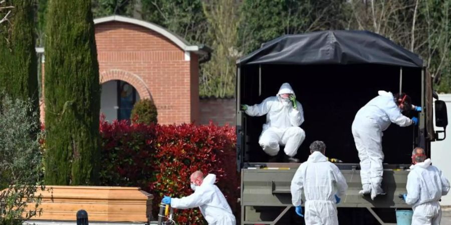 Menschen in Schutzanzügen transportieren einen Sarg auf dem Friedhof von Ferrara. Foto: Massimo Paolone/LaPresse via ZUMA Press/dpa