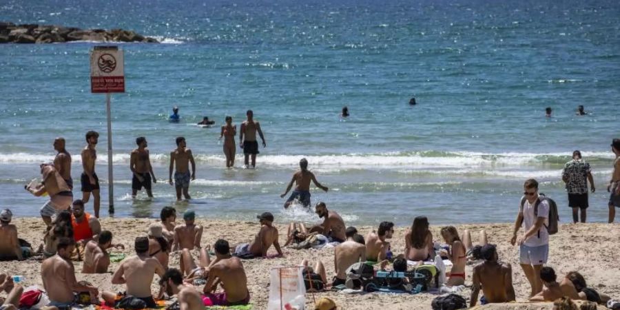Menschen verbringen den Tag in der Sonne am Strand von Tel Aviv. Foto: Ilia Yefimovich/dpa