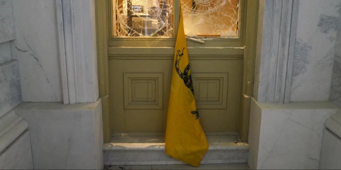 Eine Flagge hängt zwischen zerbrochenen Fenstern, nachdem Anhänger von Präsident Donald Trump im Januar 2021 versucht hatten, Polizeiabsperrungen vor dem US-Kapitol zu durchbrechen. trump kapitol