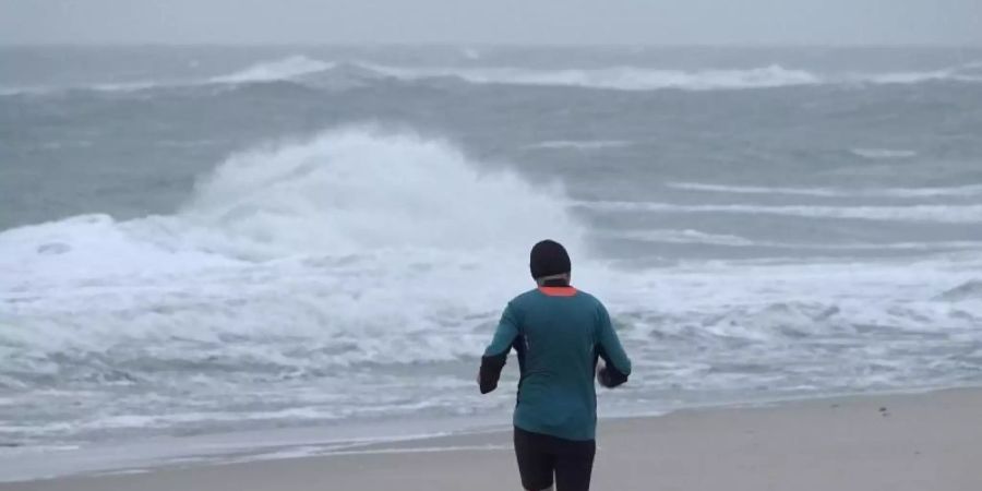 Ein Jogger ist bei stürmischem Wetter am Strand von Westerland auf Sylt unterwegs. Foto: Bodo Marks/dpa