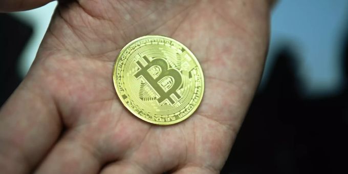 Ein Mann hält eine nachgemachte Münze mit dem Bitcoin-Logo in den Händen. dollar bitcoin