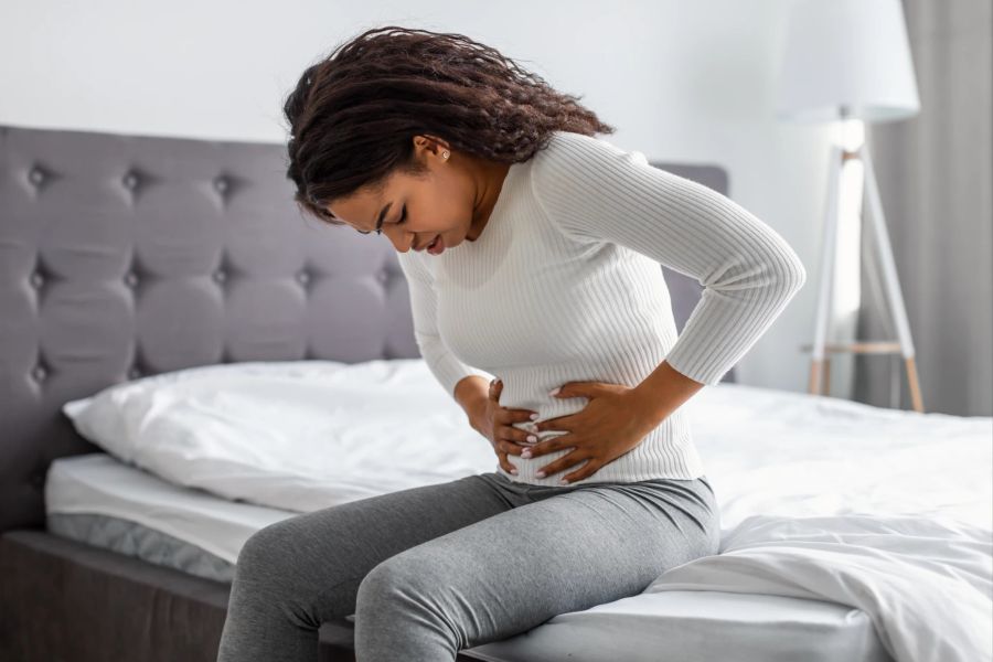 frau im bett hält sich bauch