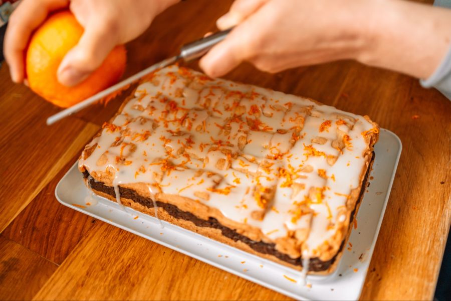 Person reibt Orangenschale auf einen Kuchen