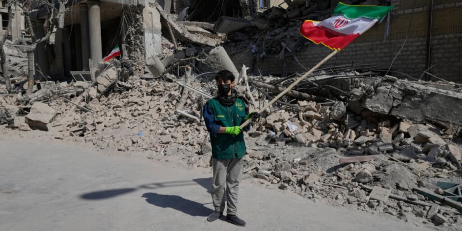 dpatopbilder - Ein Junge schwenkt eine iranische Flagge vor einer Polizeieinrichtung, die während der amerikanisch-israelischen Militäraktion  getroffen wurde. Foto: Vahid Salemi/AP/dpa