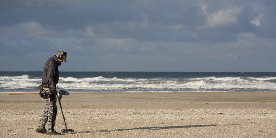 Mann mit Metalldetektor am Strand