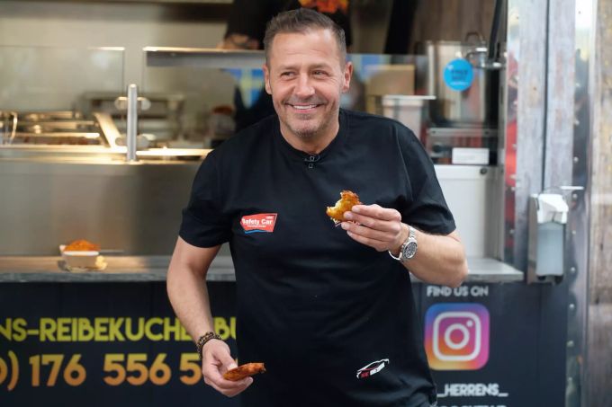 Schauspieler und Reality-Star Willi Herren isst bei der Eröffnung von ·Willi Herren·s Rievkooche Bud· in die Kamera einen Reibekuchen. Schauspieler Willi Herren