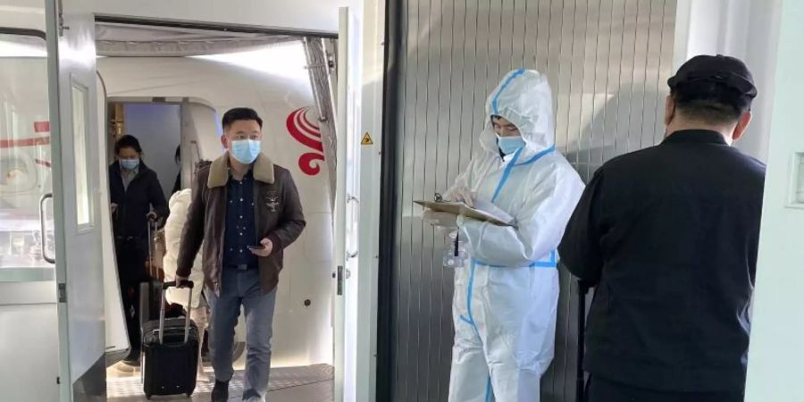 Passagiere tragen Schutzmasken und verlassen ein Flugzeug nach der Ankunft am Wuhan Tianhe International Airport. Foto: Ng Han Guan/AP/dpa
