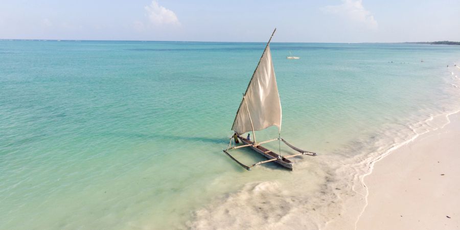 Dhow-Katamaran-Segelboot verlässt weissen Sandstrand ins blaue Meer.