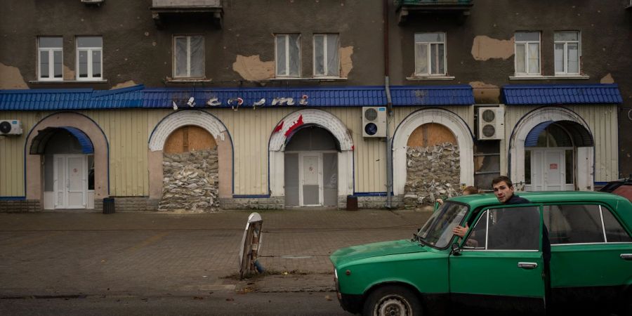 Menschen schieben ein liegengebliebenes Fahrzeug an einem stillgelegten Restaurant vorbei.