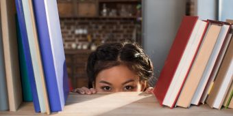 asiatische frau schaut vor bücherregal hervor