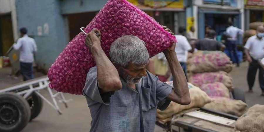 Ein Mann trägt einen Sack mit importierten Zwiebeln auf einem Markt in Colombo. Foto: Eranga Jayawardena/AP/dpa