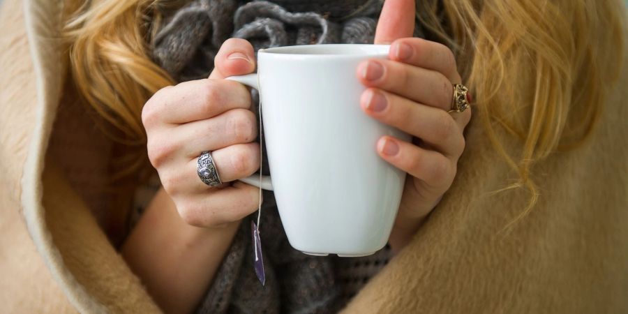 Eine Frau wärmt sich in Hannover, in eine Decke gehüllt, an einer Tasse Tee. Ab wann jemand friert, hängt von vielen Faktoren ab.