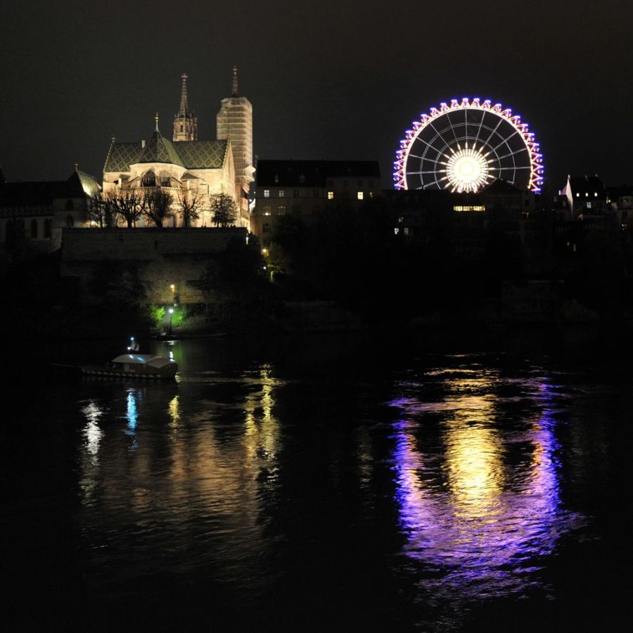 Das Basler Riesenrad strahlt in der Nacht vom Münsterplatz über den Rhein.