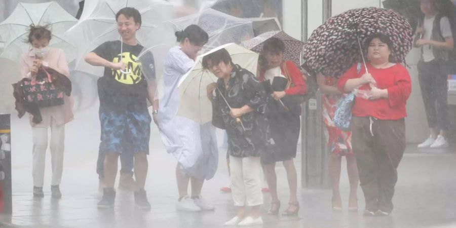 Japan, Nagoya: Menschen warten bei starkem Regen unter Regenschirmen an einer Ampel.