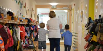 Eine Erzieherin geht in einem Kindergarten mit zwei Kindern über den Flur.