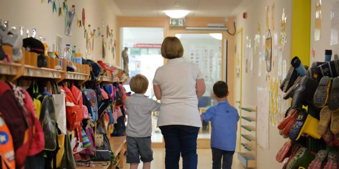 Eine Erzieherin geht in einem Kindergarten mit zwei Kindern über den Flur.
