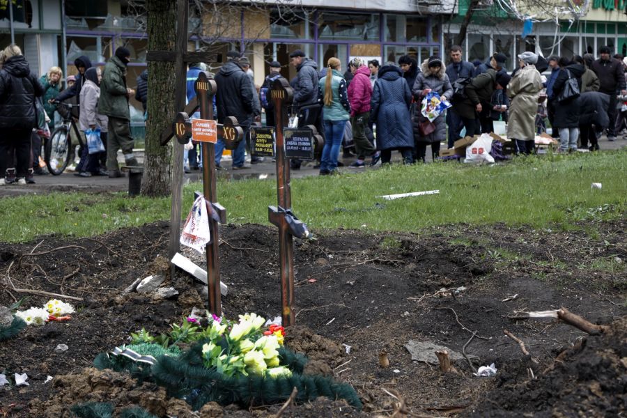 Anwohner versammeln sich auf einem behelfsmässigen Strassenmarkt neben zwei frischen Gräbern in Mariupol.