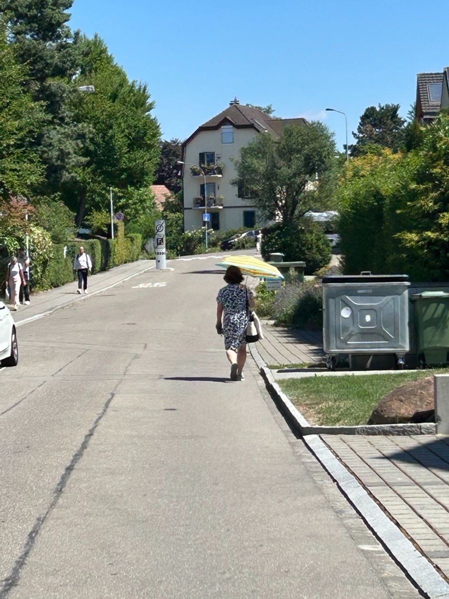 In Urdorf ZH spaziert eine Dame mit Schirm in der Mittagshitze über den heissen Asphalt.