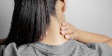 Frau fasst sich in den Nacken, Nackenschmerzen