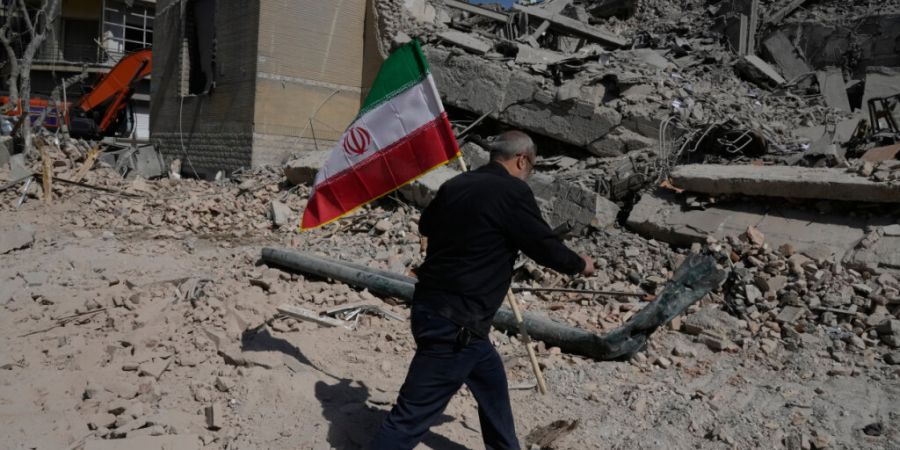 Ein Mann trägt eine iranische Flagge und legt sie auf die Trümmer einer Polizeieinrichtung, die während der amerikanisch-israelischen Militäraktion  getroffen wurde. Foto: Vahid Sal...