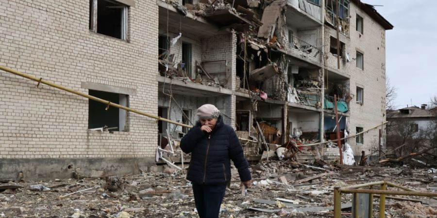 HANDOUT - Auf diesem vom Pressedienst der 65. Mechanisierten Brigade der Ukraine zur Verfügung gestellten Foto geht eine Einheimische an einem zerstörten Wohnhaus vorbei, das nach ein...