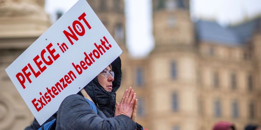 Bei einer Protestaktion vor dem Schweriner Landtag hält eine Teilnehmerin ein Schild mit der Aufschrift «Pflege in Not - Existenzen bedroht!».