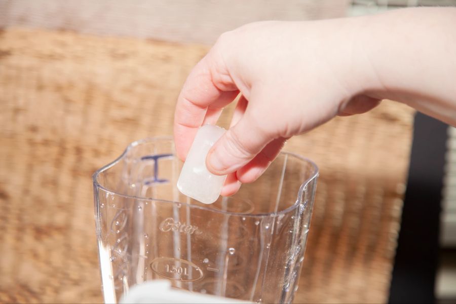 Hand gibt Eiswürfel in Mixer