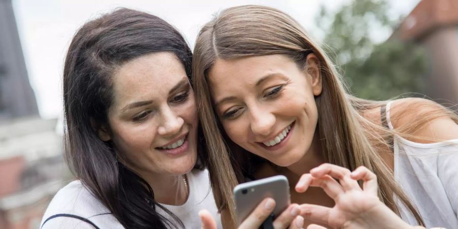 Frauen lächeln und gucken auf das Smartphone.