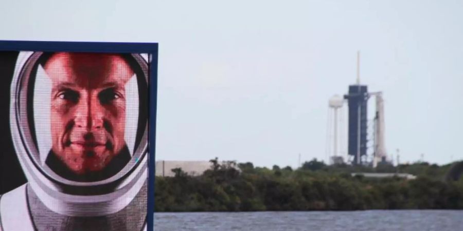 Matthias Maurer auf einem Video-Bildschirm vor dem Launchpad 39A in Cape Canaveral, an dem schon die Falcon-9-Rakete mit Crew Dragon-Kapsel aufgestellt ist. Foto: Christina Horsten/dpa