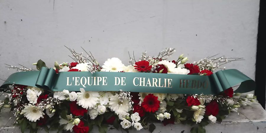 Ein Blumenkranz mit der Aufschrift «Das Team von Charlie Hebdo» liegt vor dem ehemaligen Bürogebäude des Satiremagazins. Foto: Michel Euler/POOL AP/AP/dpa