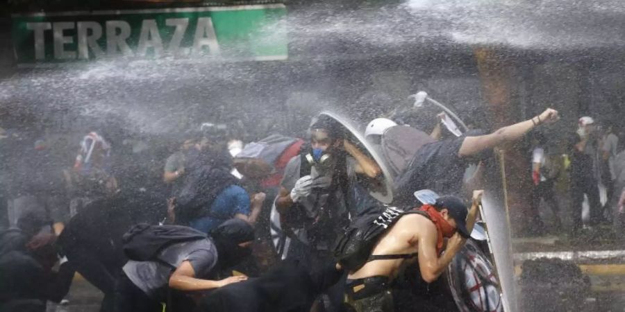 Demonstranten schützten sich in Santiago de Chile vor einem Wasserwerfer. Foto: Mario Davila/Agencia Uno/dpa