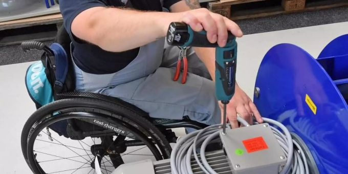An einem Arbeitsplatz für Motorklemmen ist ein Mitarbeiter im Rollstuhl mit Montagearbeiten beschäftigt. Foto: Hendrik Schmidt/zb/dpa zug