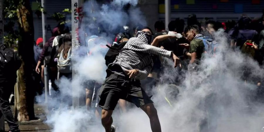 Ein Demonstrant wirft bei Protesten in Santiago de Chile eine Tränengasgranate zurück auf Polizisten. Foto: Miguel Arenas/AP/dpa