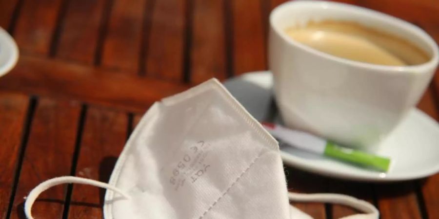 Eine FFP2-Maske liegt neben einer Tasse Kaffee auf einem Tisch. (Archivbild). Foto: Matthias Bein/dpa-Zentralbild/dpa