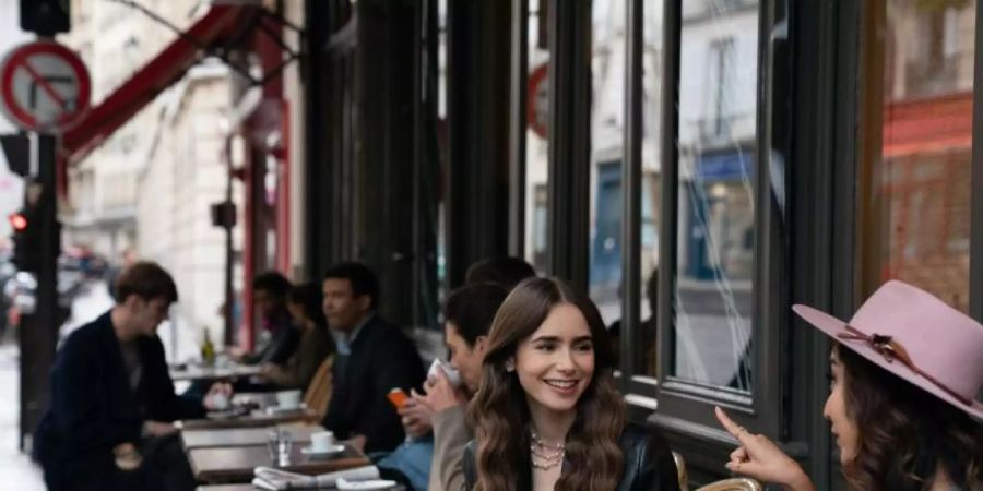 Emily (Lily Collins, m) sitzt mit einer Freundin im Café - Filmszene aus der ersten Staffel der Netflix-Serie «Emily in Paris». Foto: Stephanie Branchu/Netflix © 2020/dpa