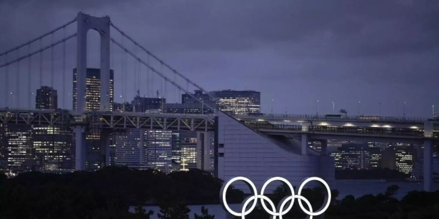 Die Olympischen Ringe leuchten in der Abenddämmerung. Foto: Felipe Dana/AP/dpa