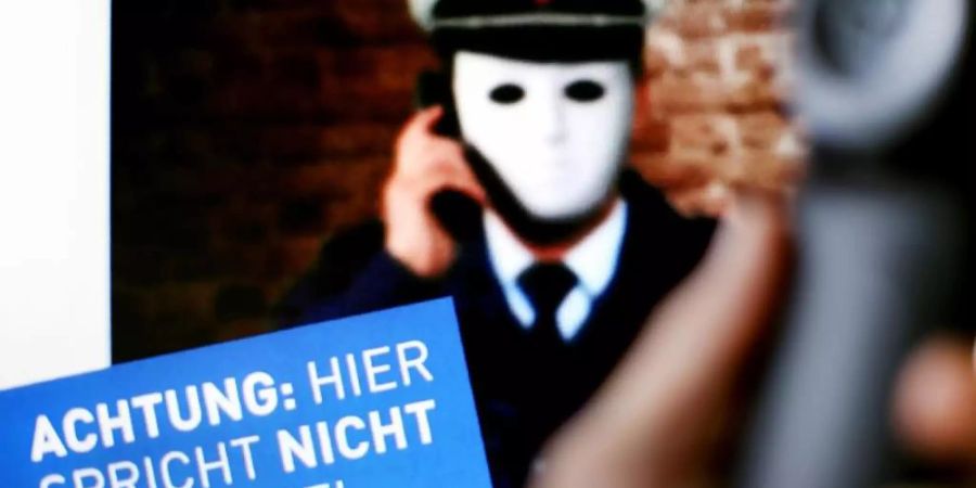 Ein Telefonhörer ist vor einem Plakat der Polizei NRW mit der Aufschrift «Achtung: Hier spricht NICHT die Polizei» zu sehen. Foto: Martin Gerten