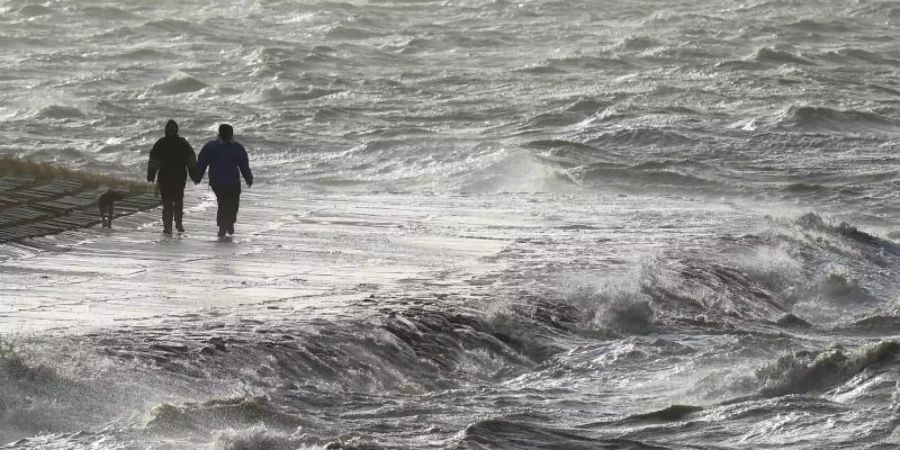 Passanten trotzen am Nordseedeich dem Sturm. Foto: Carsten Rehder/dpa