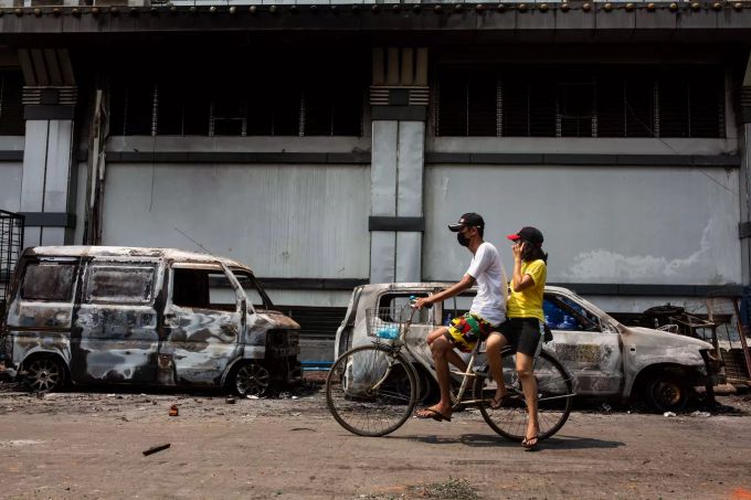 Ein Paar auf einem Fahrrad fährt an zerstörten Autos vorbei, die zuvor von Sicherheitskräften während einer Anti-Putsch-Demonstration abgebrannt wurden. Militärputsch in Myanmar