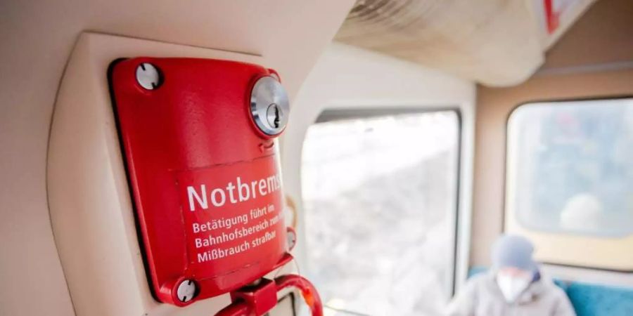 Ein Fahrgast mit Mund-Nasen-Schutz sitzt in einer Berliner S-Bahn hinter der Notbremse. Foto: Christoph Soeder/dpa