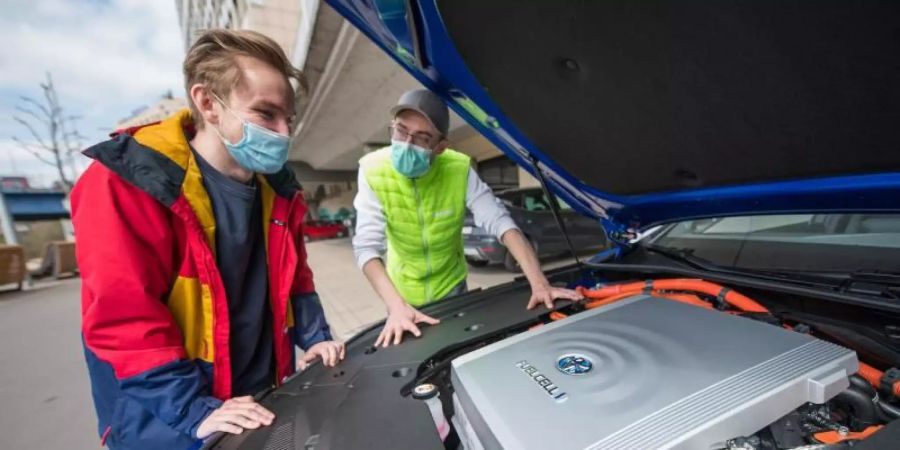 Fahrlehrer Rouven Klein (r) und Fahrschüler Adrian Bredebusch schauen auf die Brennstoffzelle des Wasserstoff-Fahrschulautos der Fahrschule VooVooDrive in Saarbrücken. Foto: Oliver Dietze/dpa
