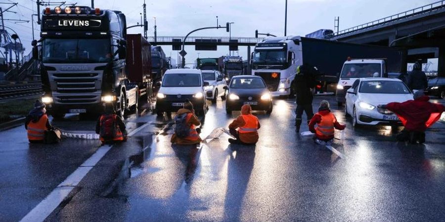 Klimaaktivisten der Aktion «Aufstand der letzten Generation» blockierten am Montagmorgen in Hamburg eine Kreuzung am Zollamt Waltershof zur Köhlbrandbrücke und zur Autobahn A7. Foto: Christi