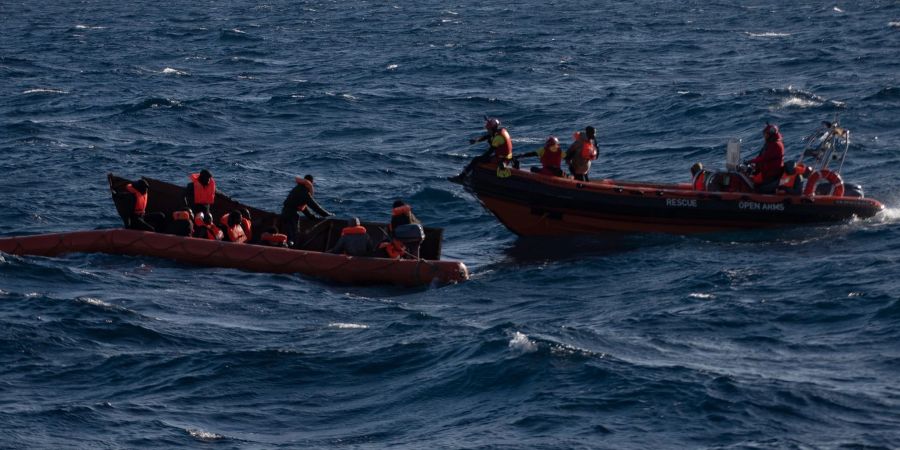 Mehrere Migranten sitzen in einem Boot im Mittelmeer während Rettungskräfte versuchen ihnen zu helfen.