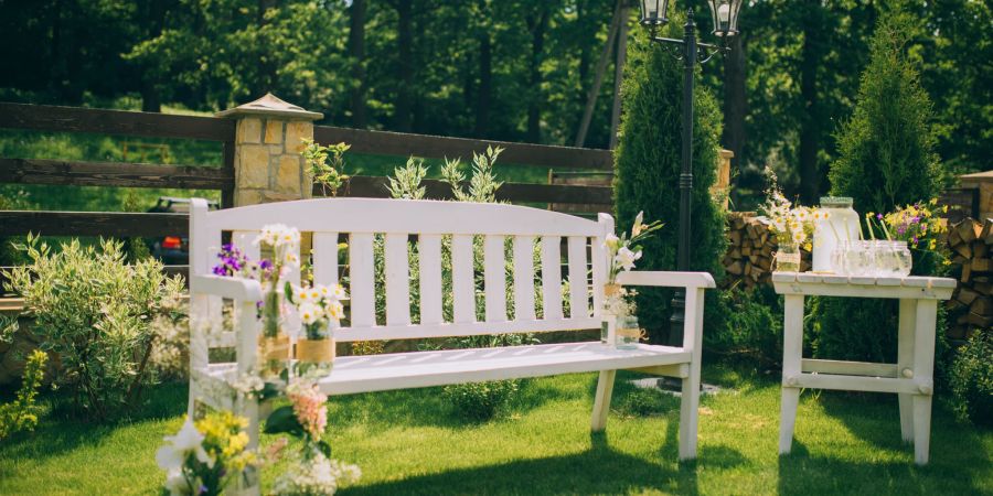 Weisse Gartenbank mit kleinem Tisch im Garten