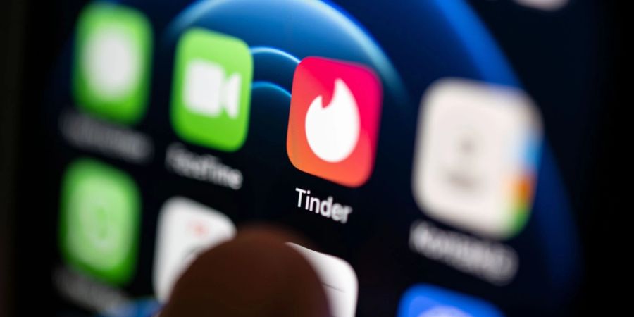 Ein Finger bedient ein Smartphone auf dem unter anderen die App von Tinder installiert ist.