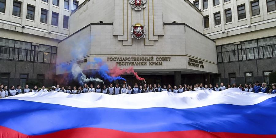 Menschen halten eine russische Nationalflagge vor dem Parlament der Krim. Foto: Uncredited/AP/Archiv