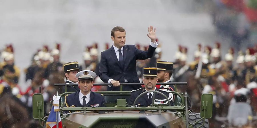 ARCHIV - Der französische Präsident Emmanuel Macron (M) wird in einem Militärfahrzeug bei einer Parade über die Champs-Elysees in Paris gefahren. Frankreich verzichtet wegen der Corona-Krise auf die traditionelle Militärparade am Nationalfeiertag 14. Juli. Foto: Michel Euler/Pool AP/dpa