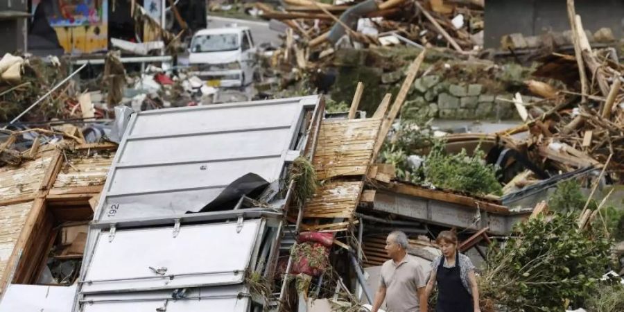 Ein Paar geht durch ein Trümmerfeld. Die Zahl der Todesopfer in den von schweren Unwettern heimgesuchten Überschwemmungsgebieten im Südwesten Japans ist weiter gestiegen. Foto: -/Kyodo News/AP/dpa