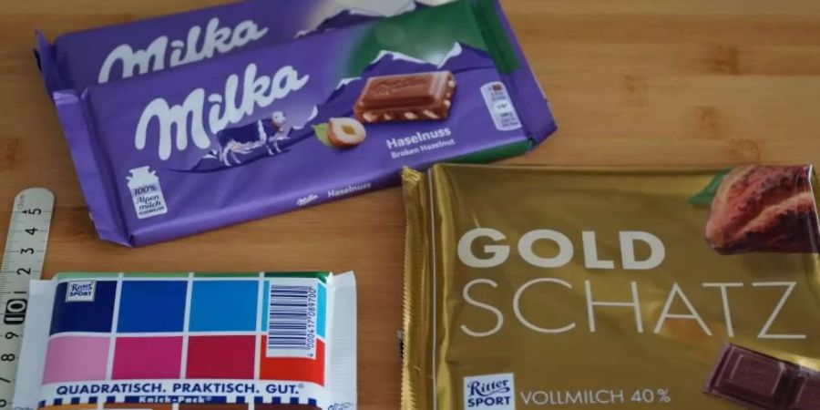 Schokoladentafeln der Marken Ritter Sport und Milka liegen neben einem Massstab auf einem Tisch. Foto: Alexander Blum/dpa